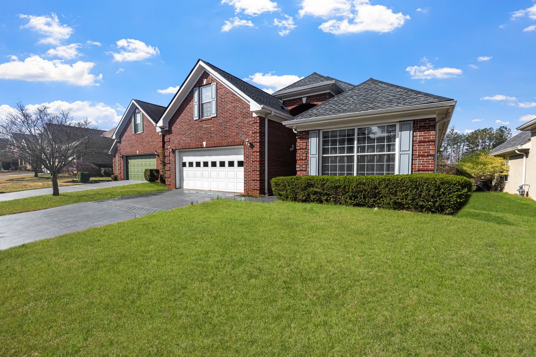 A red brick suburban house with a two-car garage and a mowed front lawn
